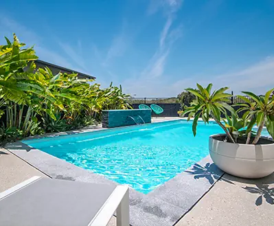 view of a swimming pool with a stunning light blue color from the side with palm tree. The pool has a waterfall feature